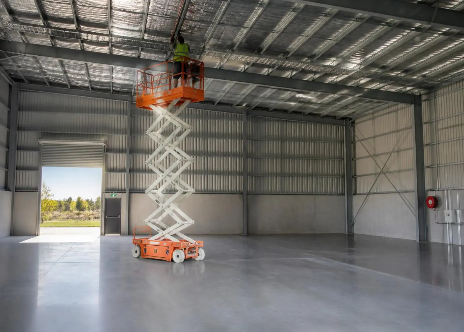 Electric scissor lift raised inside an empty steel shed during interior fit-out