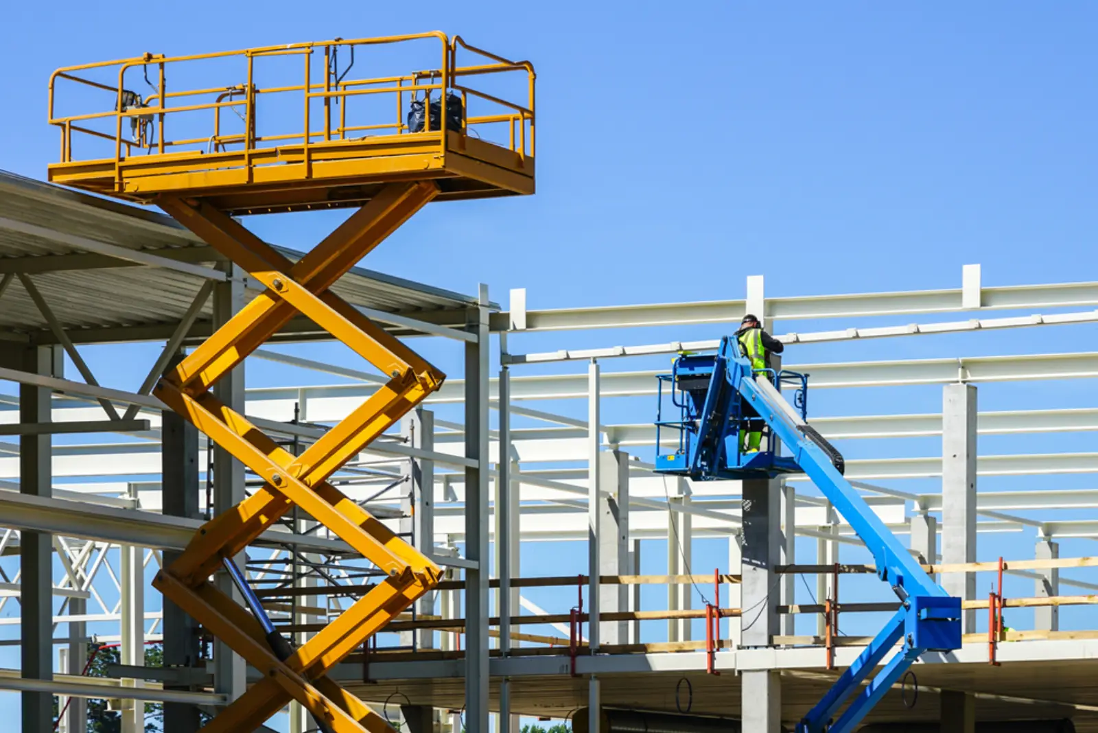 Scissor lift and boom lift with an operator in high-vis PPE working on a steel-framed building