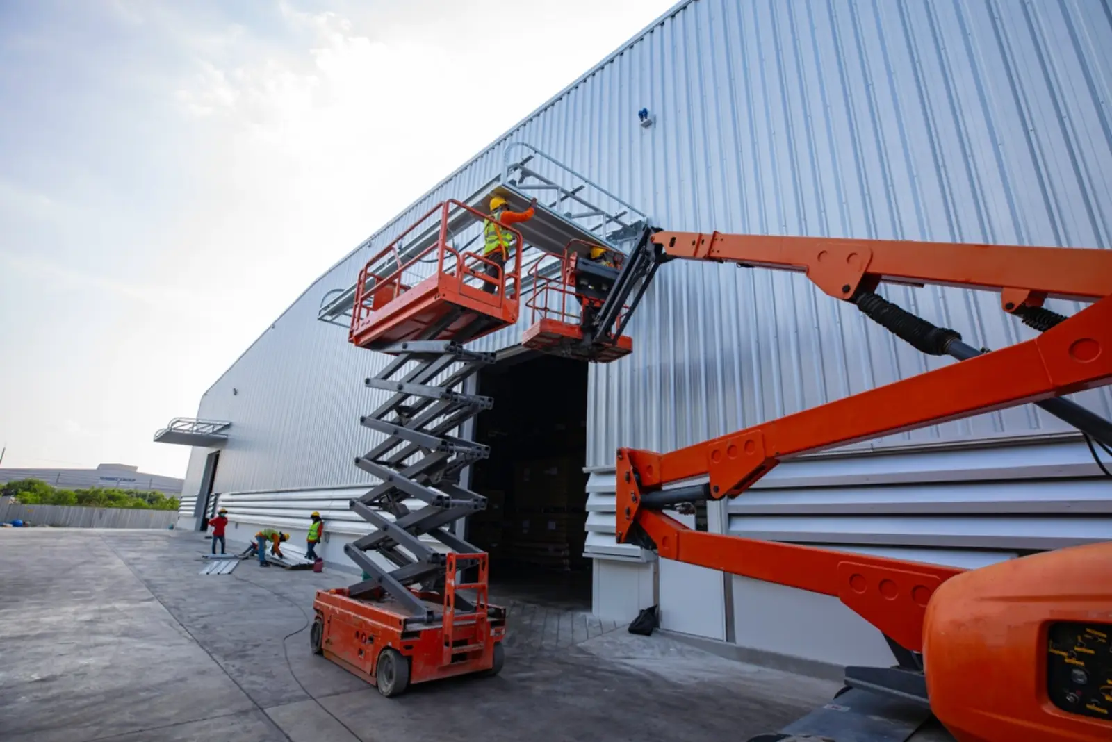 Scissor lift and boom lift in use with operators in PPE outside a steel shed build
